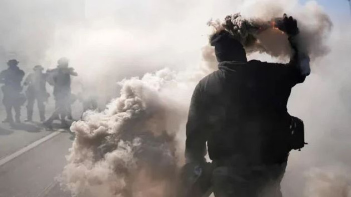 এক বিক্ষোভকারী স্মোক ক্যানিস্টার নিক্ষেপ করছেন